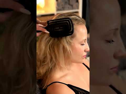 Lea gently lifts strands of the Client's hair, adjusting the weight with practiced ease as warm oil
