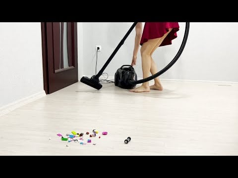 A girl in a dress using a bagless Bosch vacuum cleaner cleans the house from Lego toys